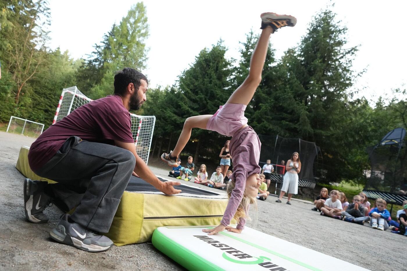 Trenér jistí dívku při parkourovém prvku na žíněnce